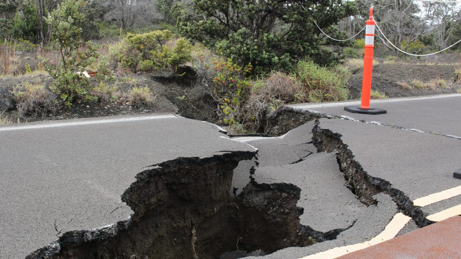 Road surface split open by an earthquake fissure, marked with a traffic cone