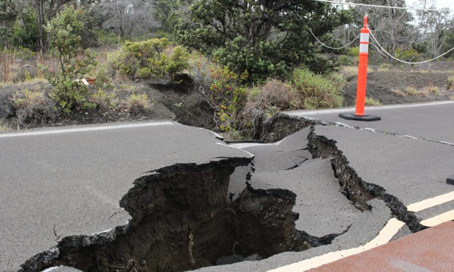 Road surface split open by an earthquake fissure, marked with a traffic cone