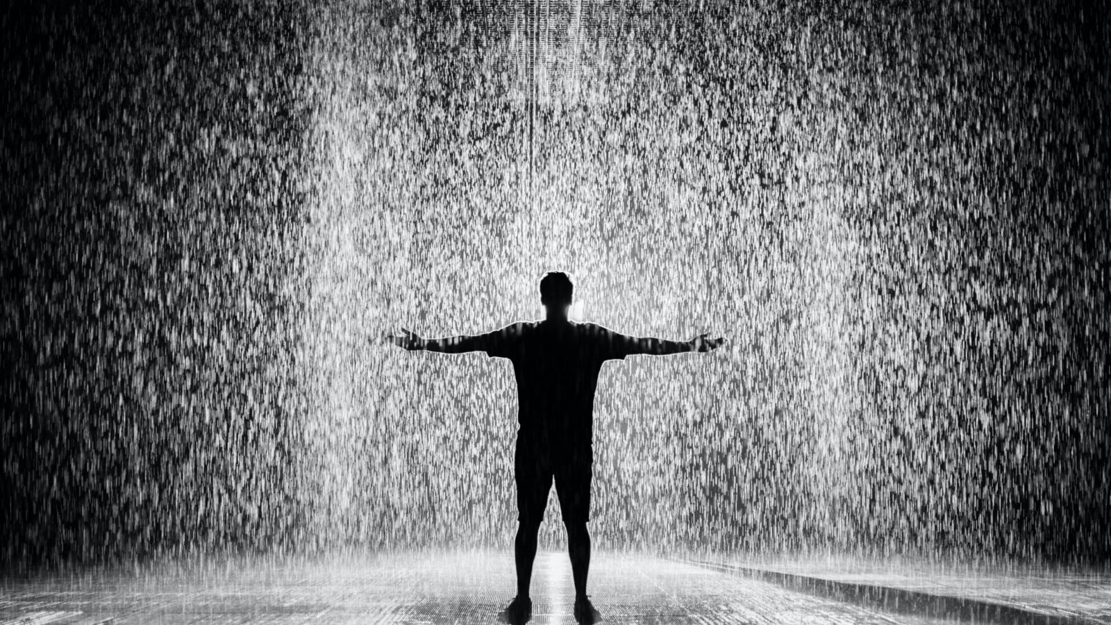 Silhouetted figure standing with arms outstretched in heavy rain
