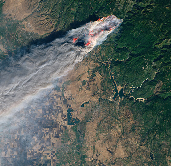 Satellite view of a wildfire trailing a long smoke plume across forested terrain