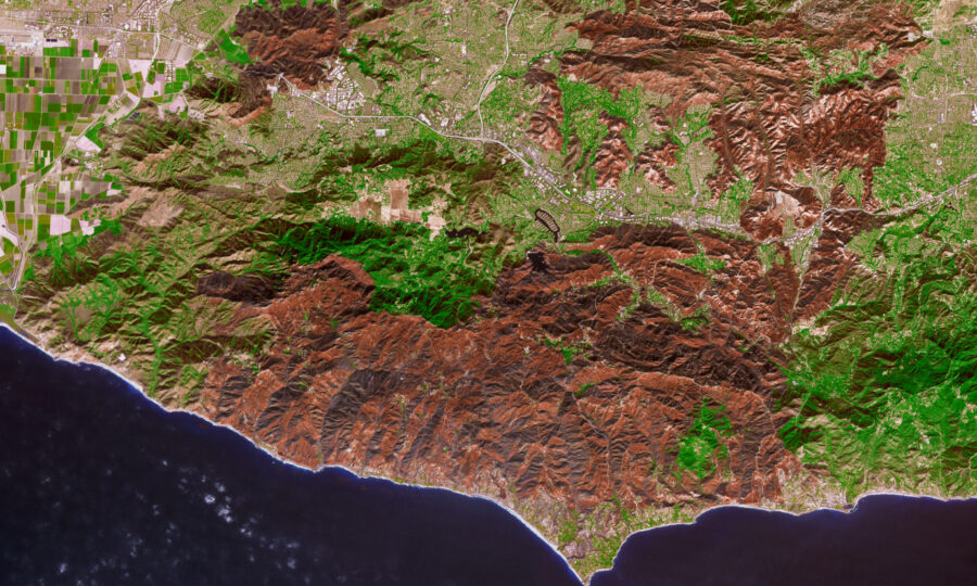 Satellite view of a dark wildfire burn scar reaching the coastline