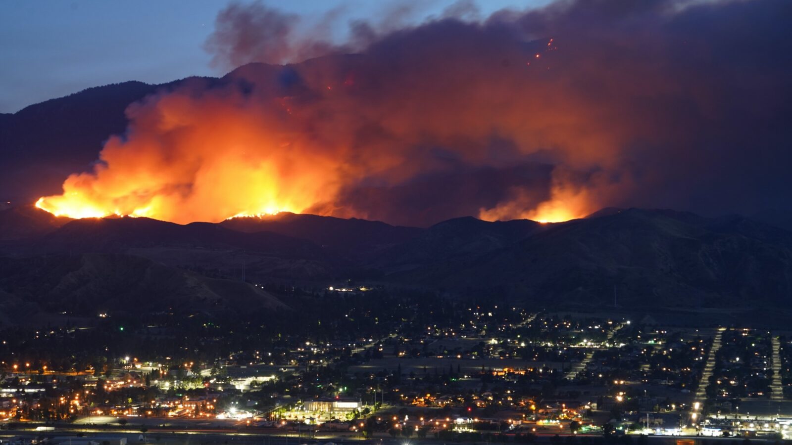 Wildfire burning along a ridgeline above a lit city at night