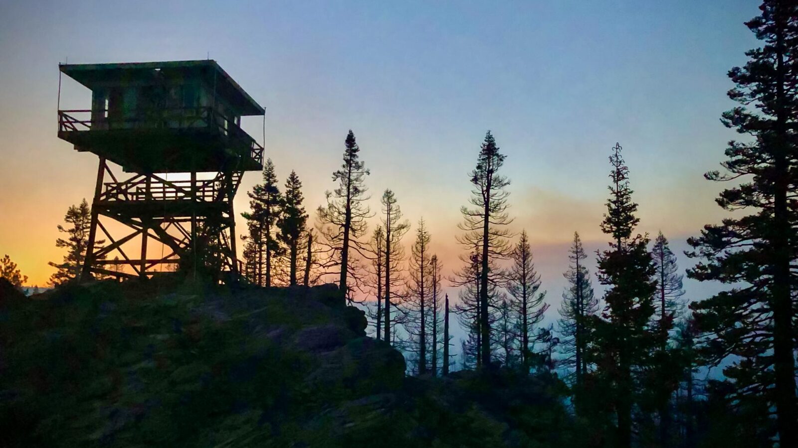 Fire lookout tower silhouetted on a forested ridge at dusk