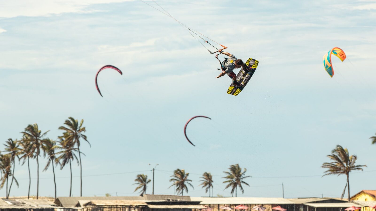 Kitesurfers lifted by strong offshore winds past a palm-lined shore