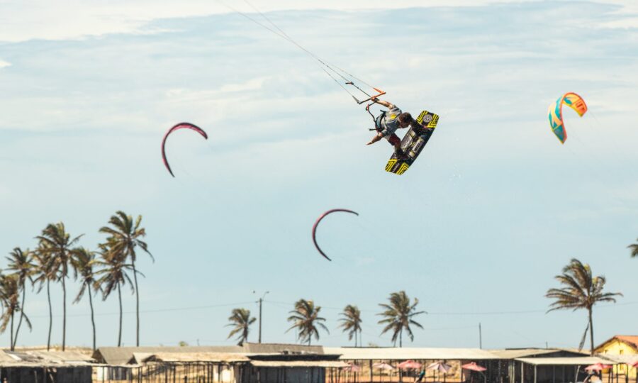 Kitesurfers lifted by strong offshore winds past a palm-lined shore