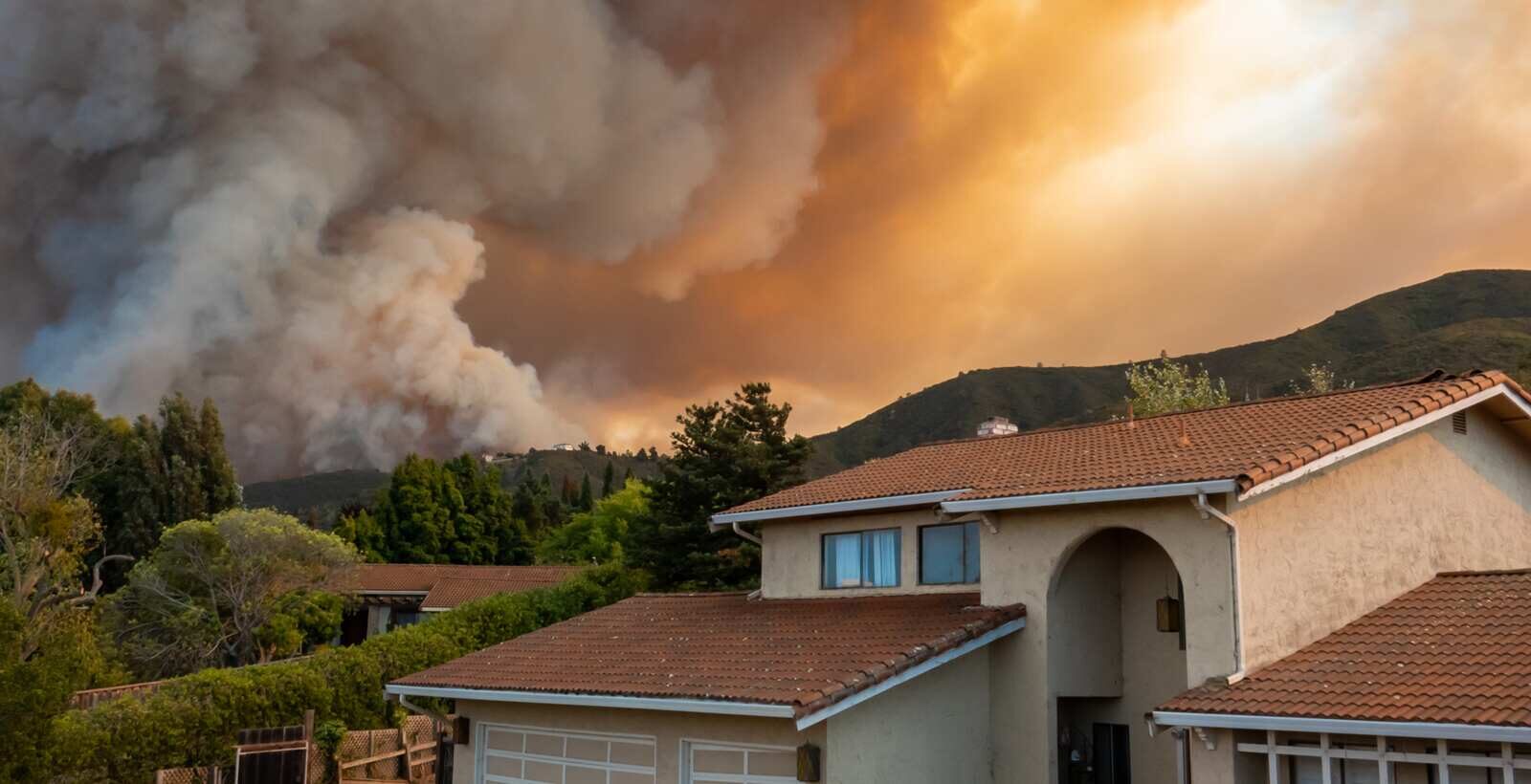 Smoke plume rising beyond the roofline of a suburban house