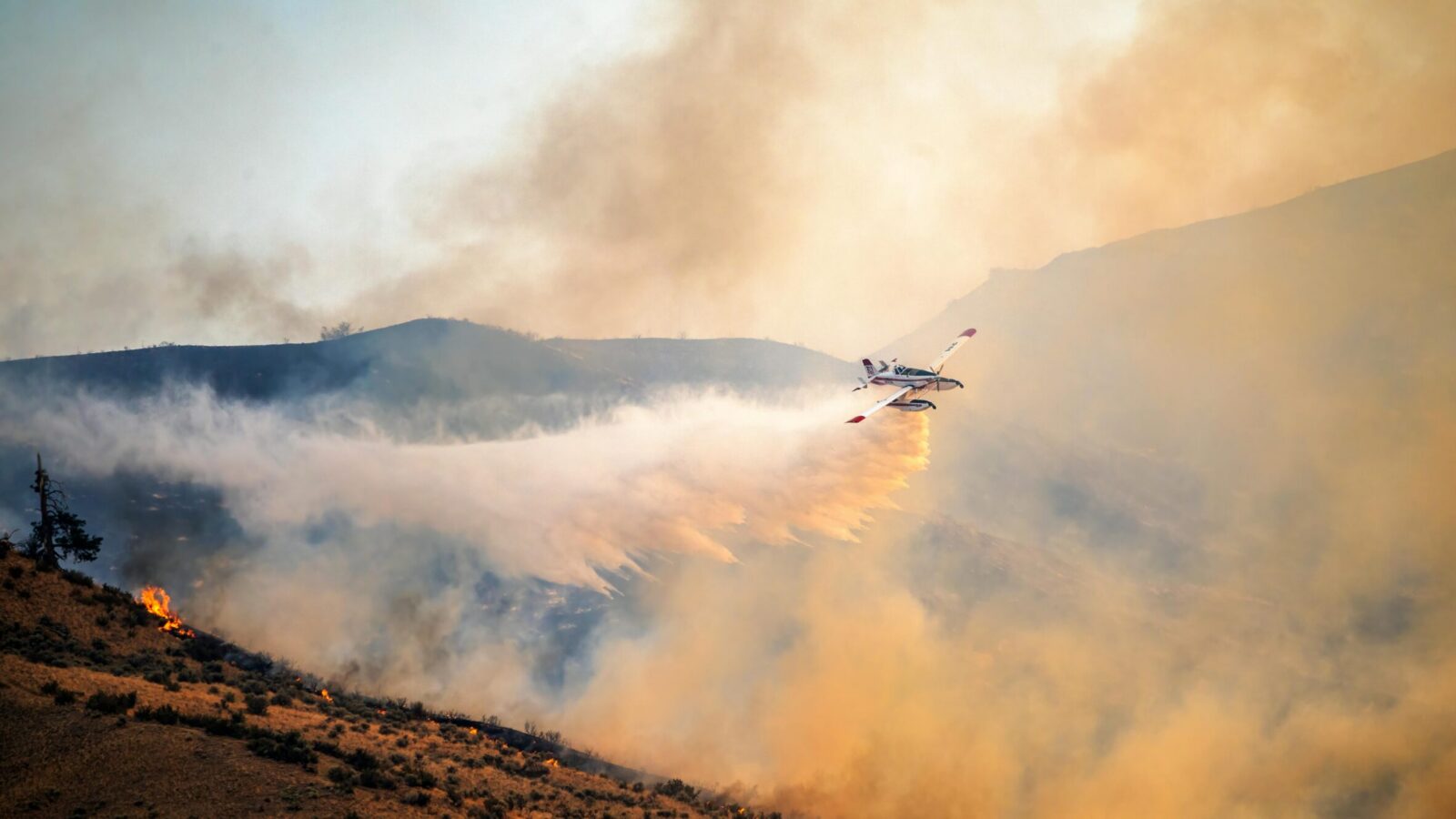 Air tanker dropping retardant along a burning hillside