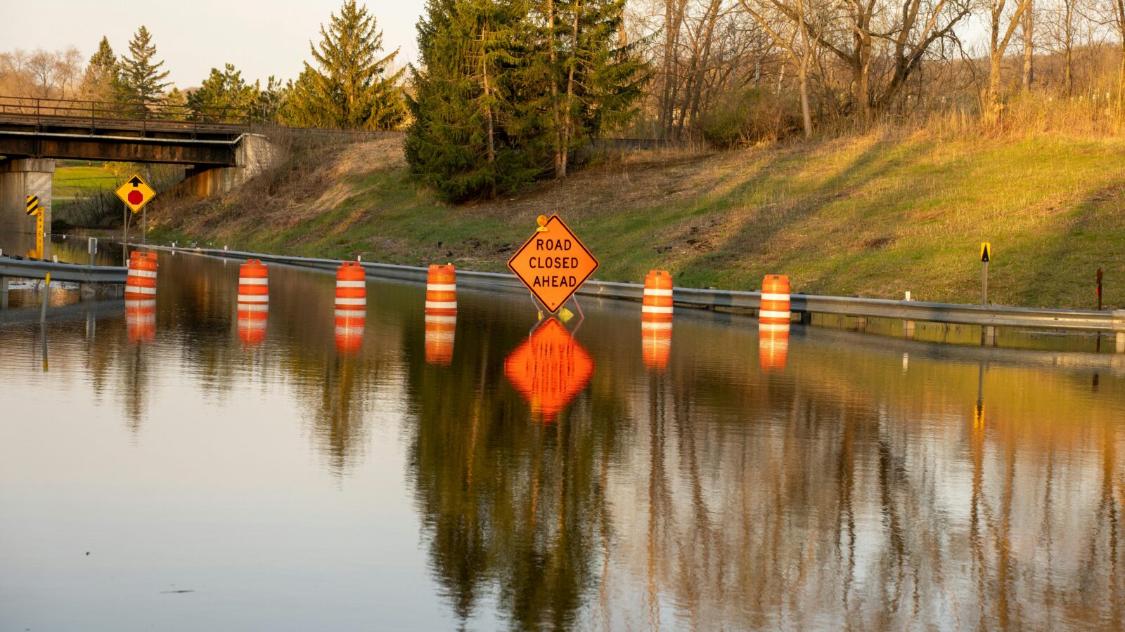 Road closed barriers standing in floodwater beside a swollen channel