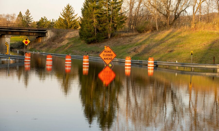 Road closed barriers standing in floodwater beside a swollen channel