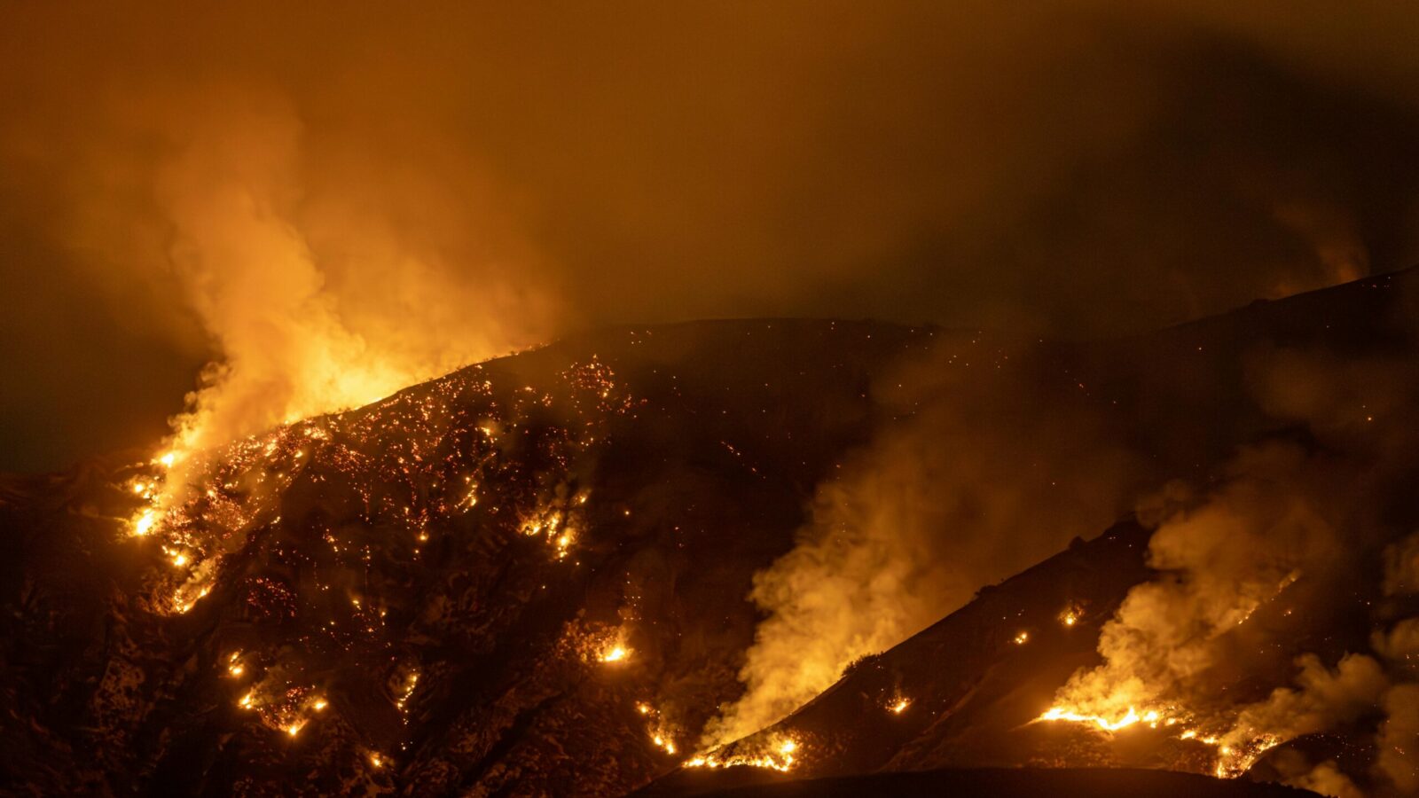 Wildfire burning in lines along a dark ridge at night